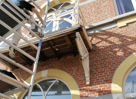 Bouwsteiger en dakrand van een bakstenen gebouw, met arbeider aan de zijkant.